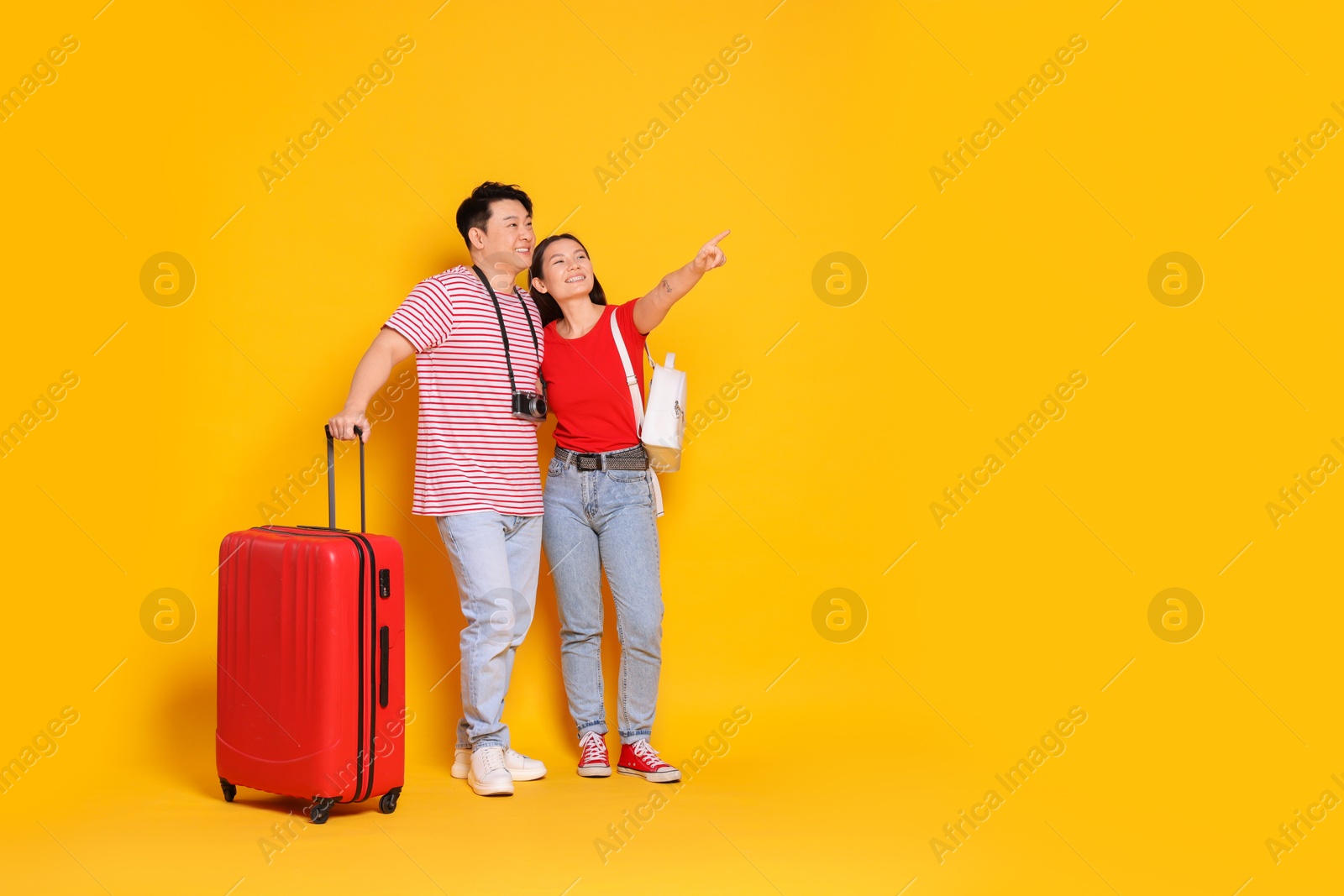 Photo of Happy travellers with suitcase pointing at something on yellow background. Space for text