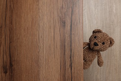 Photo of Cute knitted bear peeking out of wooden door, space for text