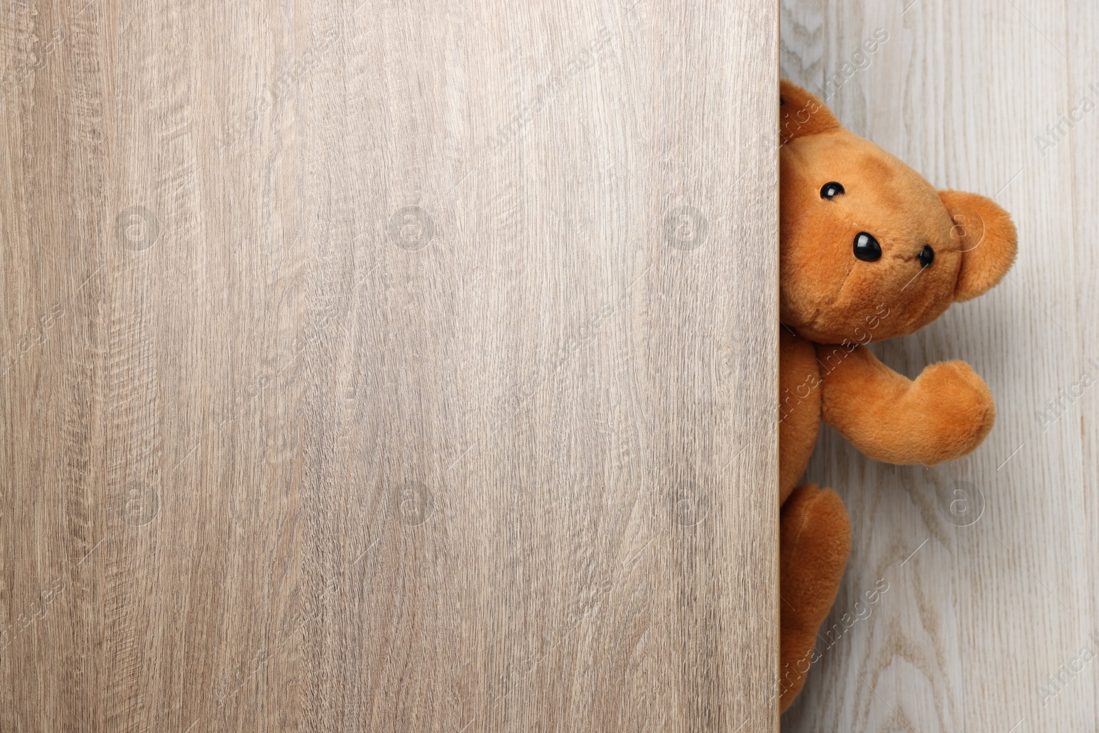 Photo of Cute teddy bear peeking out of wooden door, space for text