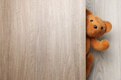 Photo of Cute teddy bear peeking out of wooden door, space for text