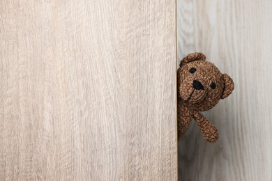 Photo of Cute knitted bear peeking out of wooden door, space for text