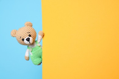 Photo of Cute knitted bear peeking out from yellow card on light blue background, space for text