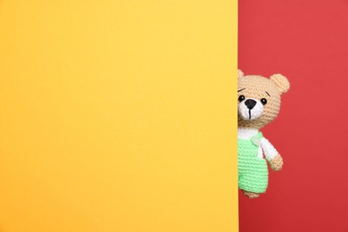 Photo of Cute knitted bear peeking out from yellow card on red background, space for text