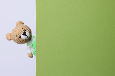 Photo of Cute knitted bear peeking out from green card on white background, space for text