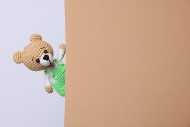 Photo of Cute knitted bear peeking out from beige card on white background, space for text