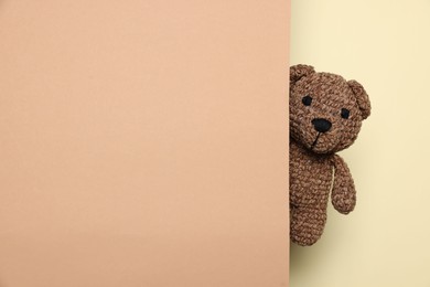 Photo of Cute knitted bear peeking out from color card on beige background, space for text