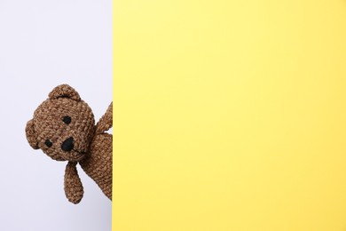 Photo of Cute knitted bear peeking out from yellow card on white background, space for text