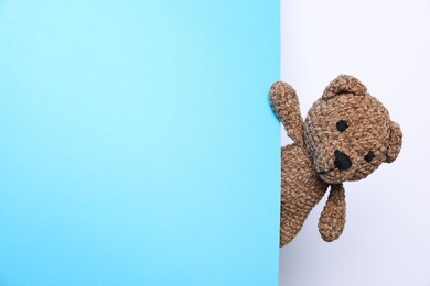 Photo of Cute knitted bear peeking out from light blue card on white background, space for text