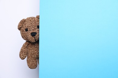 Photo of Cute knitted bear peeking out from light blue card on white background, space for text