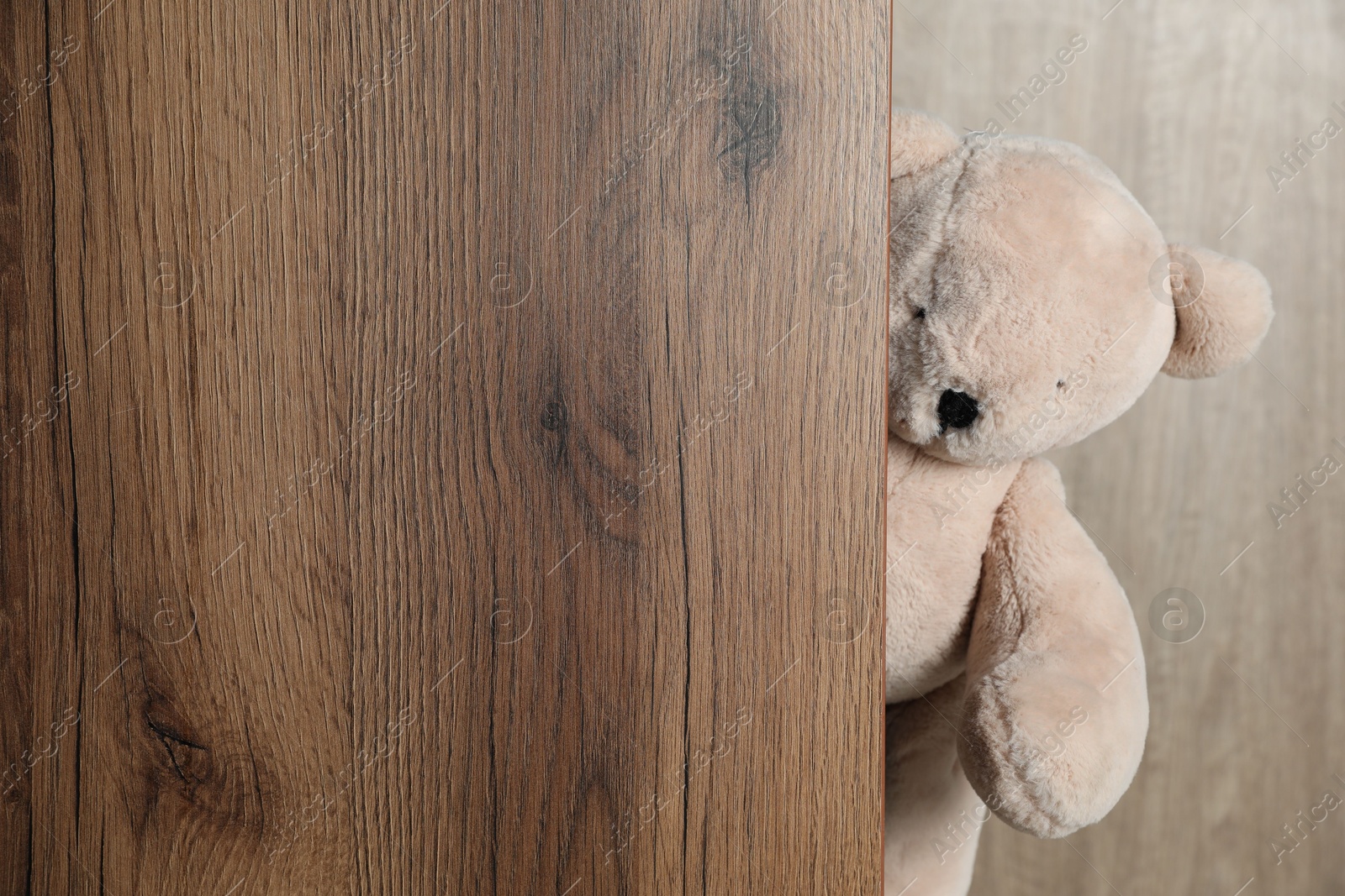 Photo of Cute teddy bear peeking out of wooden board. Space for text