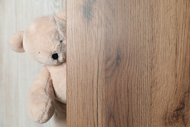 Photo of Cute teddy bear peeking out of wooden board. Space for text