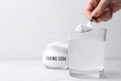 Photo of Woman adding baking soda to glass of water at white textured table, closeup. Space for text