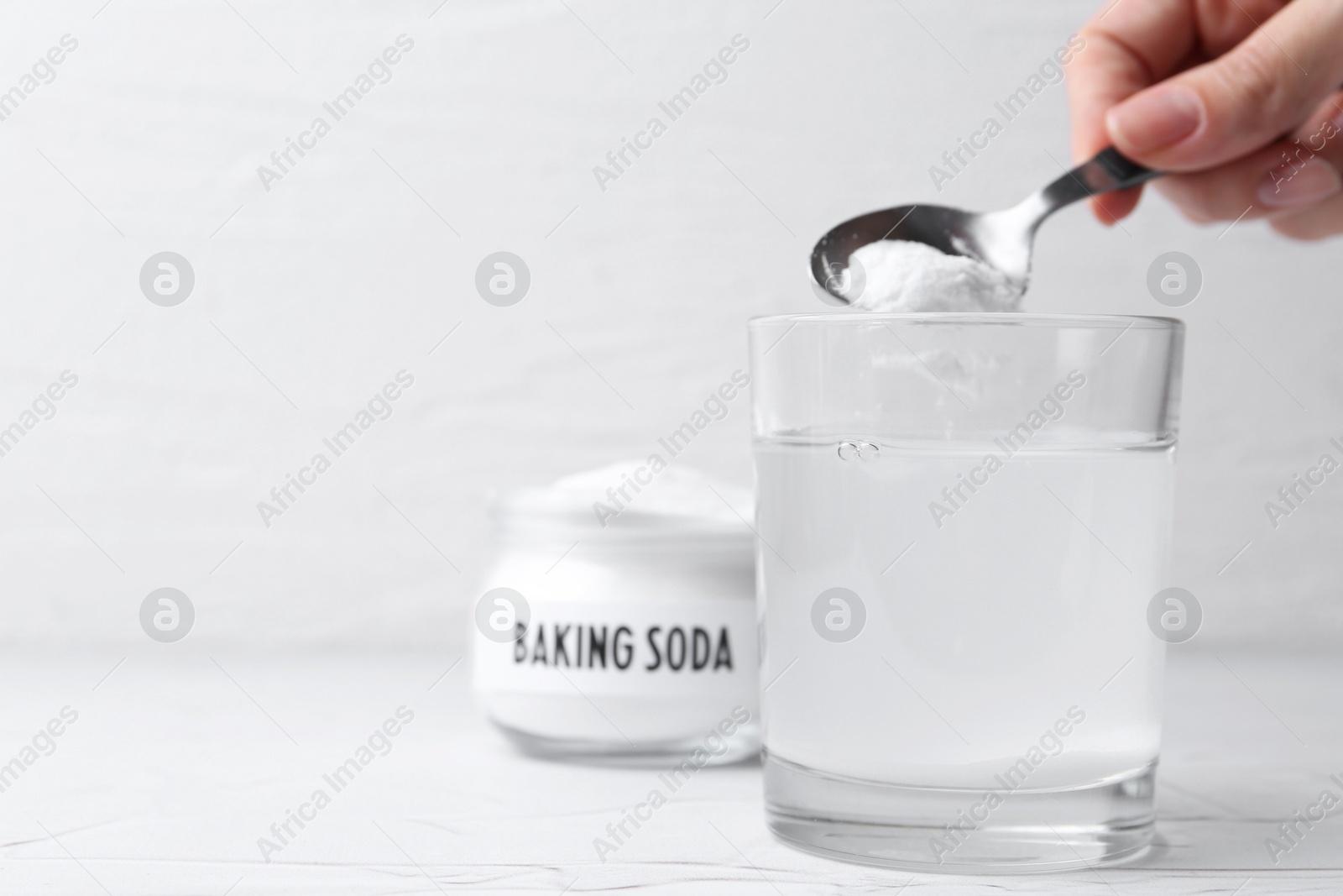 Photo of Woman adding baking soda to glass of water at white textured table, closeup. Space for text