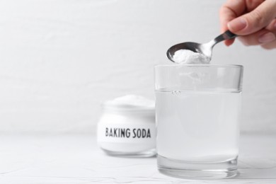 Photo of Woman adding baking soda to glass of water at white textured table, closeup. Space for text