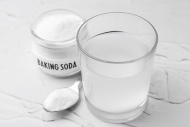 Photo of Glass with water and baking soda on white textured table, closeup