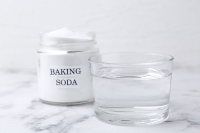 Photo of Glass of water and baking soda on white marble table, closeup