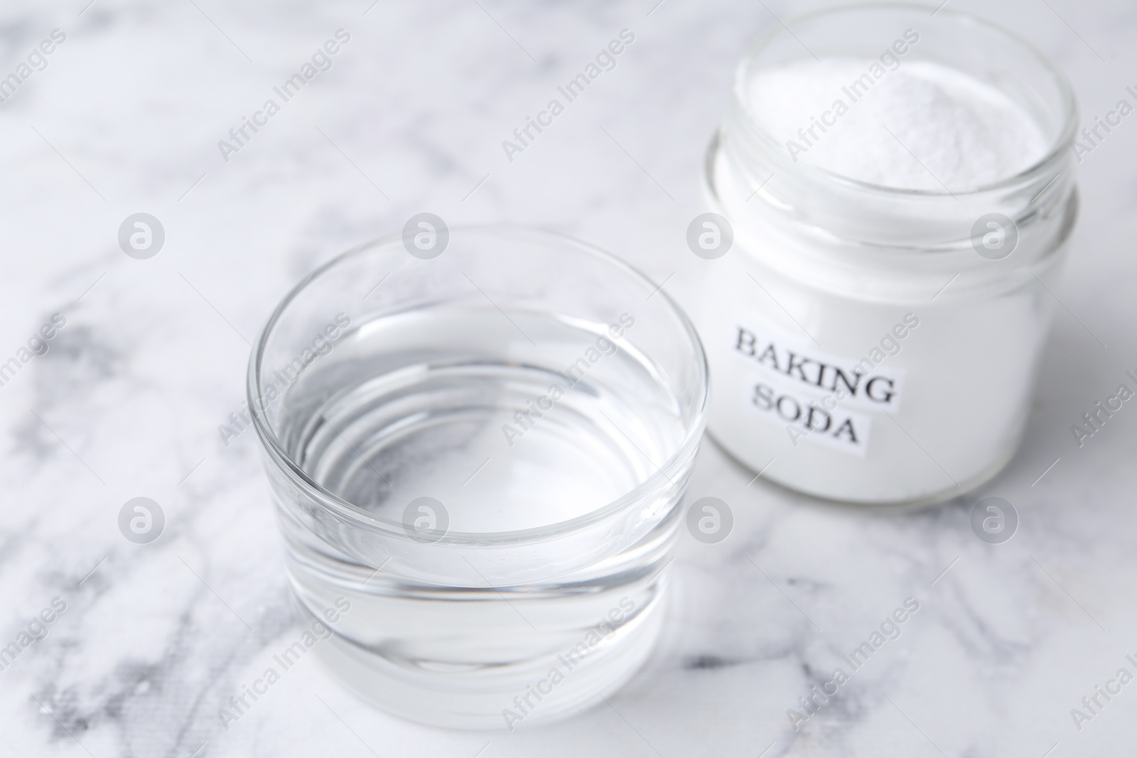 Photo of Glass of water and baking soda on white marble table, selective focus