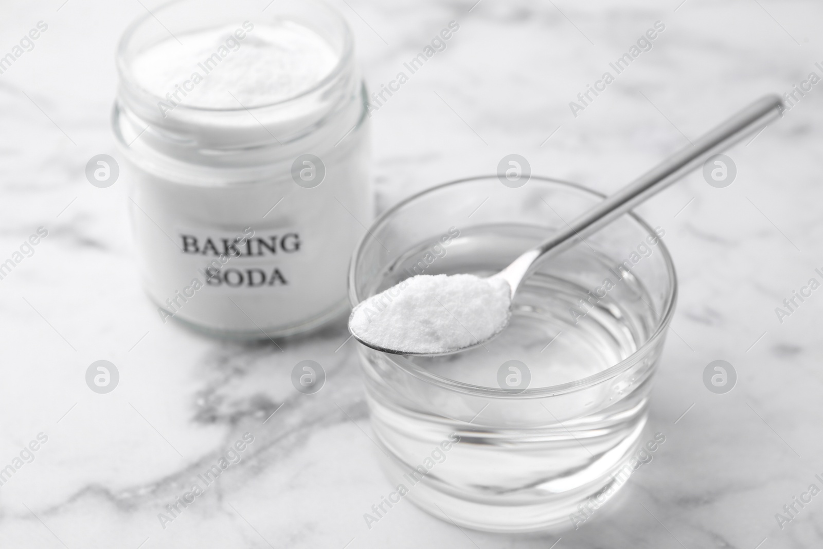 Photo of Glass of water and baking soda on white marble table, selective focus