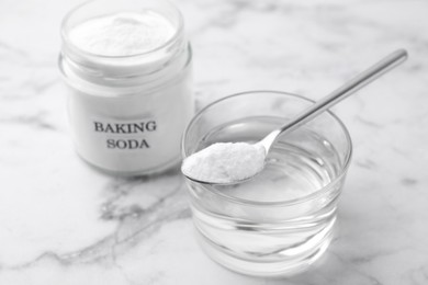 Photo of Glass of water and baking soda on white marble table, selective focus