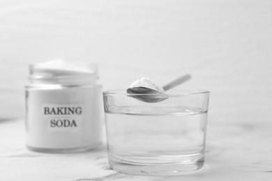 Photo of Glass of water and baking soda on white marble table, selective focus