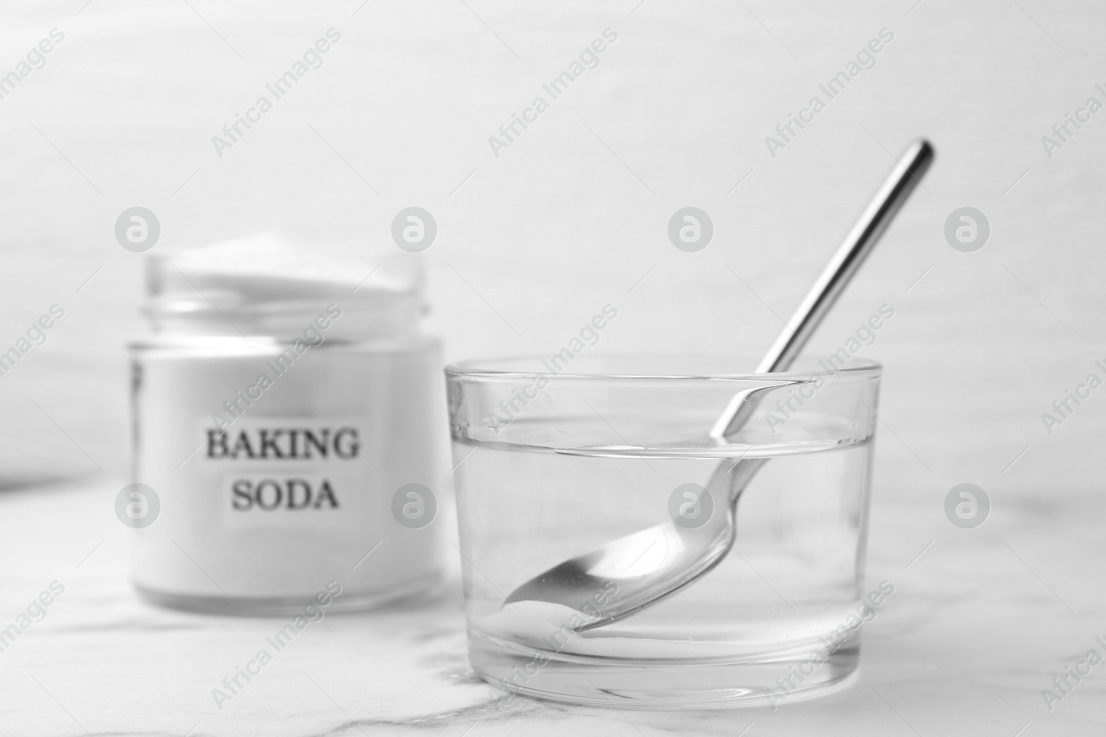 Photo of Glass of water and baking soda on white marble table, selective focus