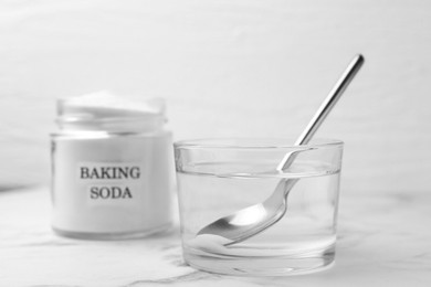 Photo of Glass of water and baking soda on white marble table, selective focus