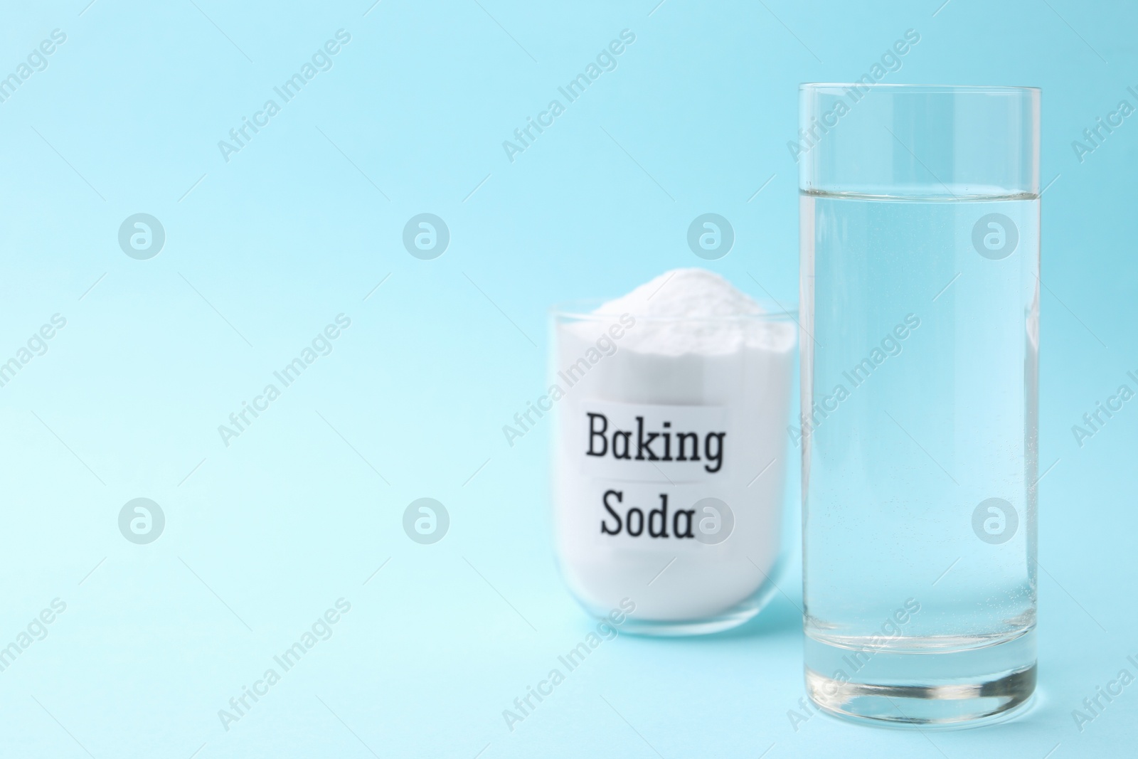 Photo of Glass of water and baking soda on light blue background. Space for text