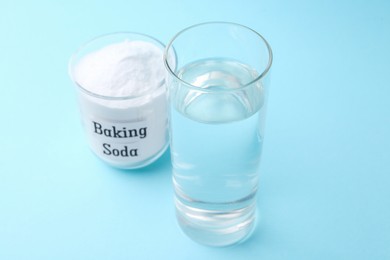 Photo of Glass of water and baking soda on light blue background