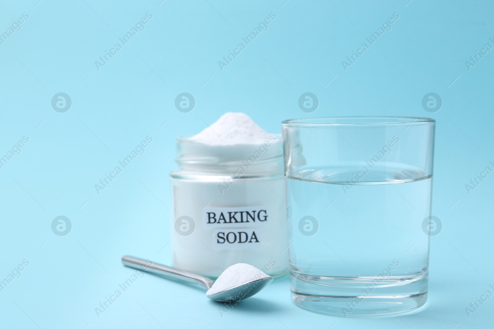 Photo of Glass of water and baking soda on light blue background. Space for text