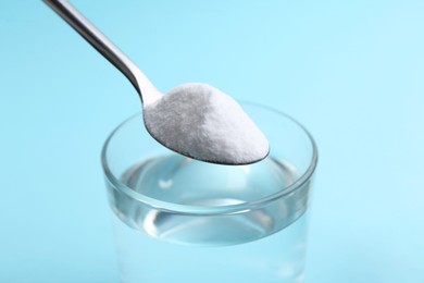 Adding baking soda to glass of water on light blue background, closeup