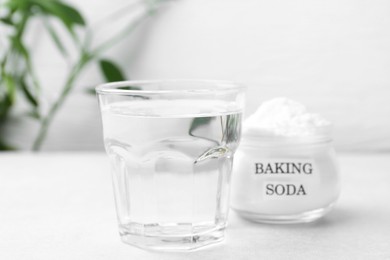 Photo of Glass of water and baking soda on white table, selective focus