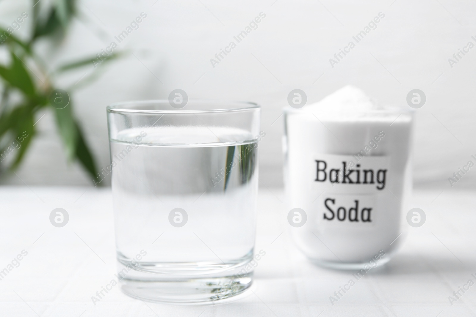 Photo of Glass of water and baking soda on white tiled table, closeup