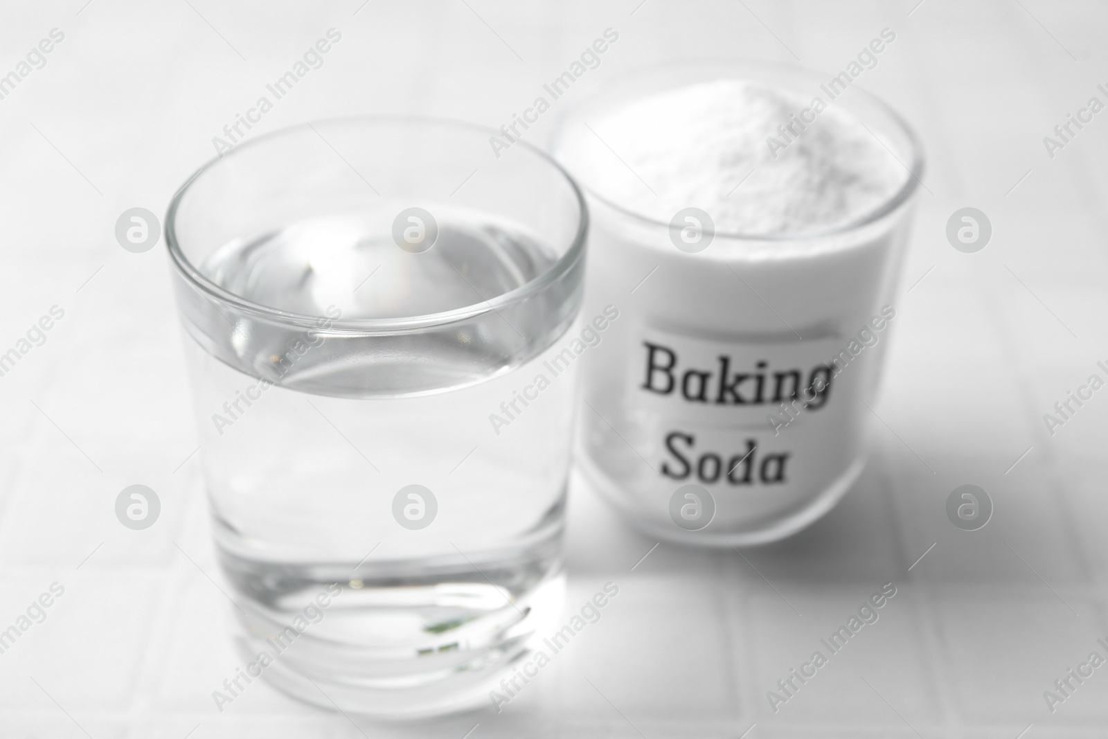 Photo of Glass of water and baking soda on white tiled table, closeup