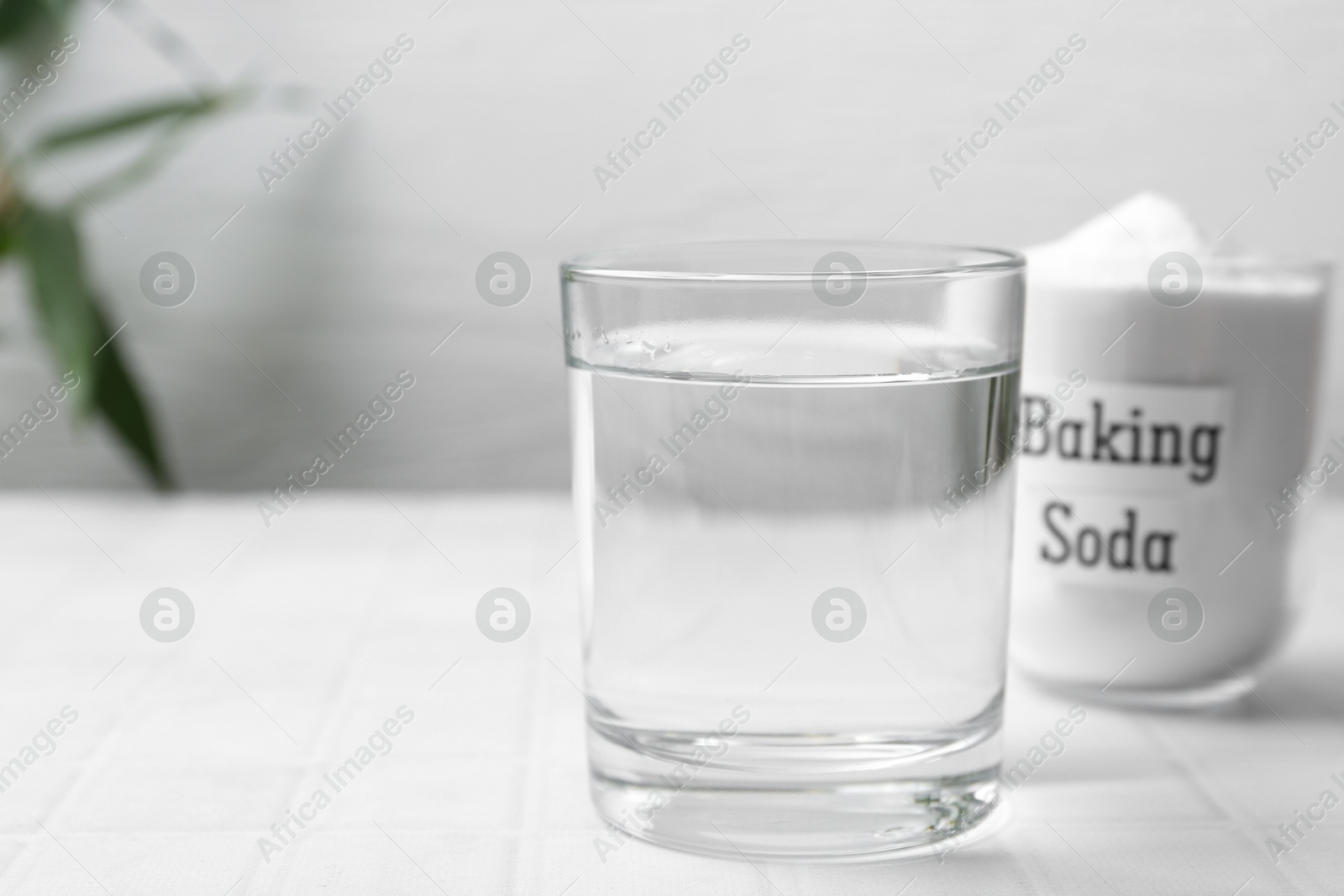 Photo of Glass of water and baking soda on white tiled table. Space for text