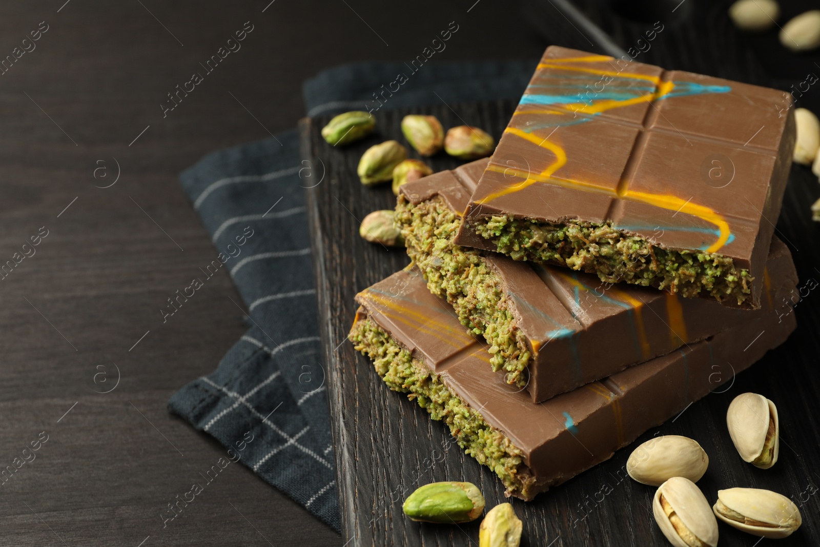 Photo of Pieces of Dubai chocolate bars with pistachios and knafeh on black wooden table, closeup. Space for text