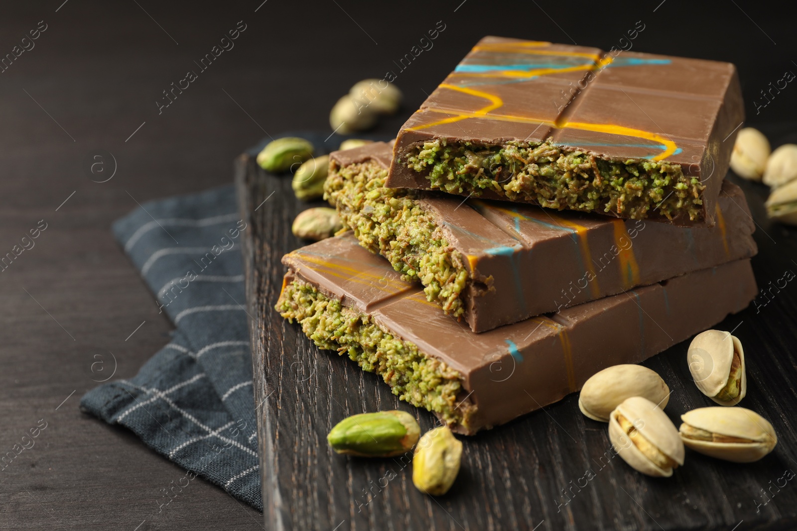 Photo of Pieces of Dubai chocolate bars with pistachios and knafeh on black wooden table, closeup