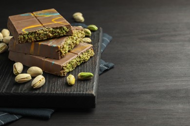 Photo of Pieces of Dubai chocolate bars with pistachios and knafeh on black wooden table, closeup. Space for text