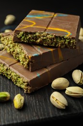 Photo of Pieces of Dubai chocolate bars with pistachios and knafeh on black table, closeup