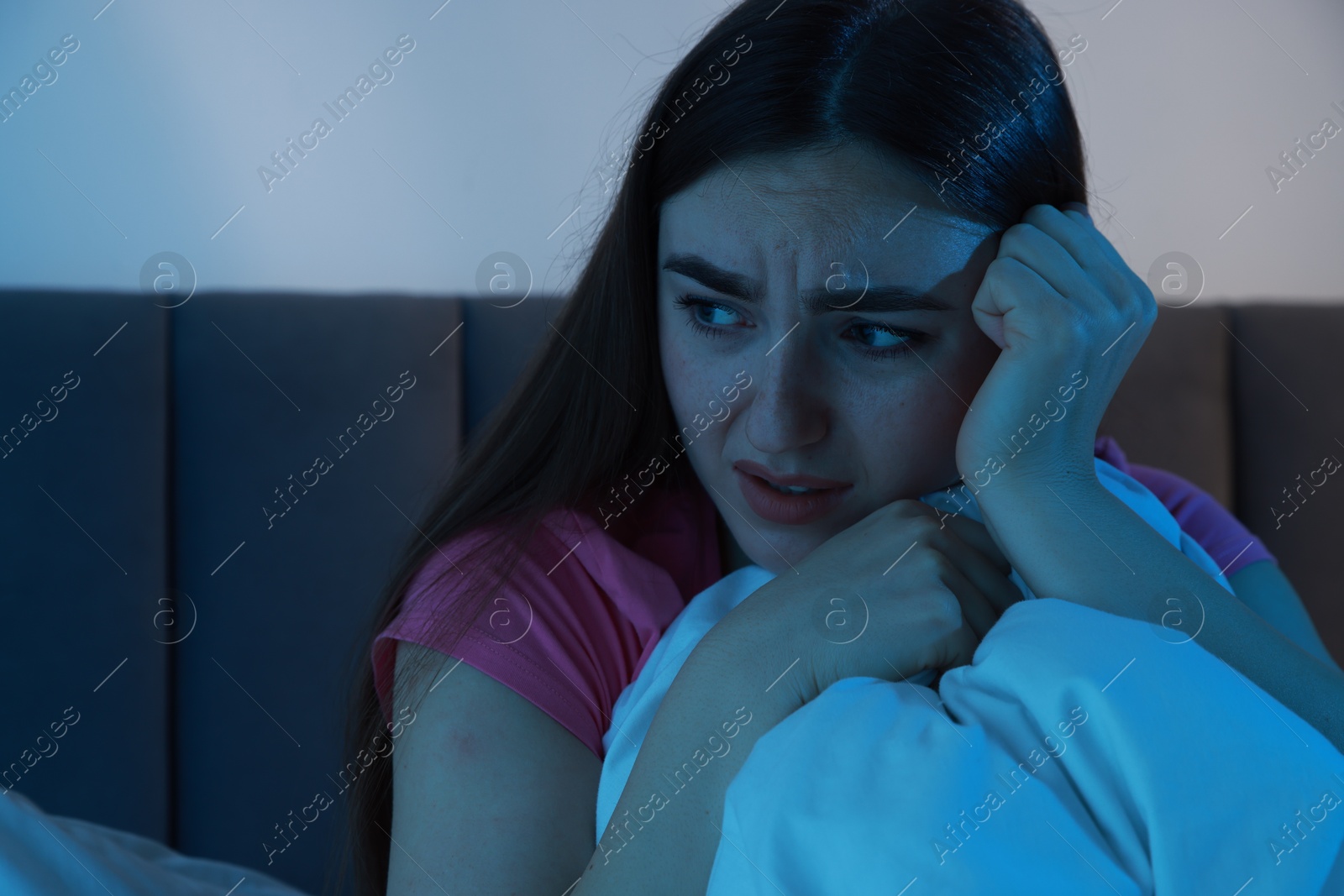 Photo of Fear of darkness. Scared young woman on bed in room at night