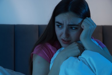 Photo of Fear of darkness. Scared young woman on bed in room at night