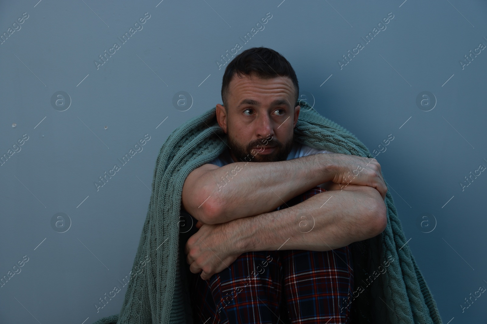 Photo of Fear of darkness. Scared man with blanket on light grey background