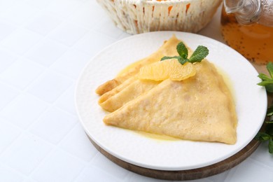 Photo of Tasty crepes Suzette on white tiled table, closeup. Space for text