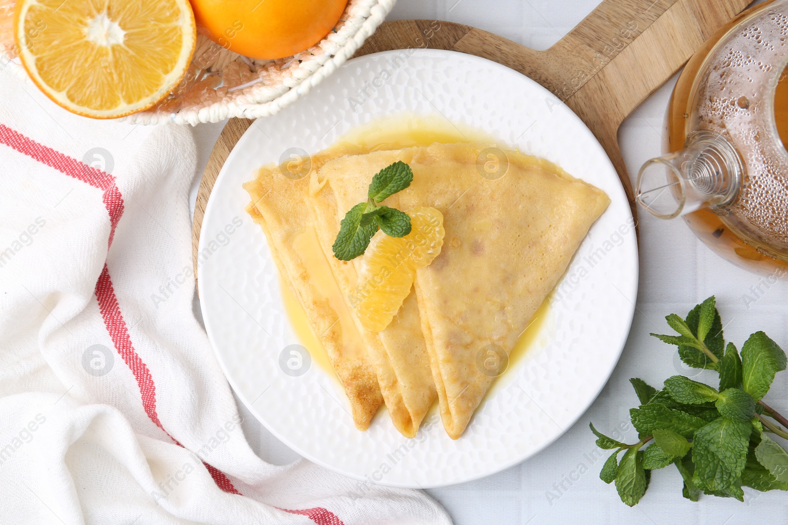 Photo of Tasty crepes Suzette and products on white tiled table, flat lay