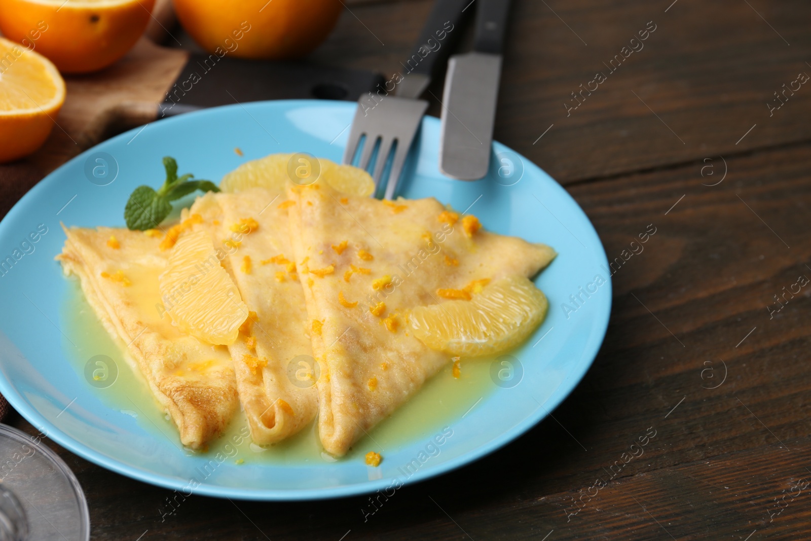 Photo of Plate with tasty crepes Suzette on wooden table, closeup