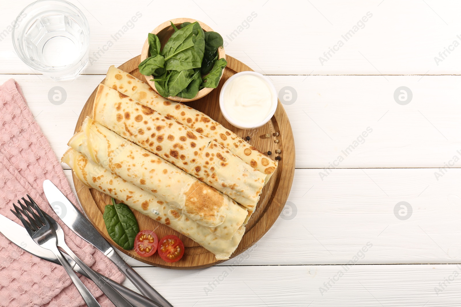 Photo of Tasty rolled crepes with cottage cheese and spinach served on white wooden table, flat lay. Space for text