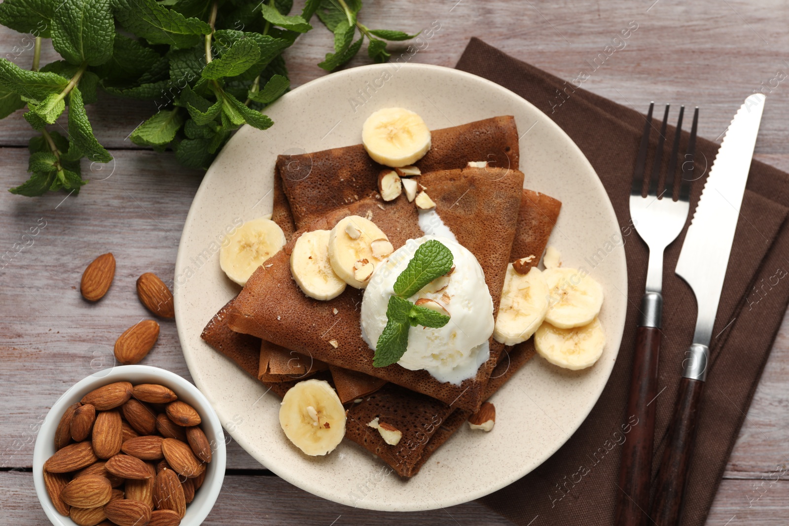 Photo of Delicious chocolate crepes with banana, nuts, mint and scoop of ice cream on wooden table, flat lay