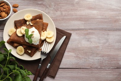 Photo of Delicious chocolate crepes with banana, nuts, mint and scoop of ice cream on wooden table, flat lay. Space for text