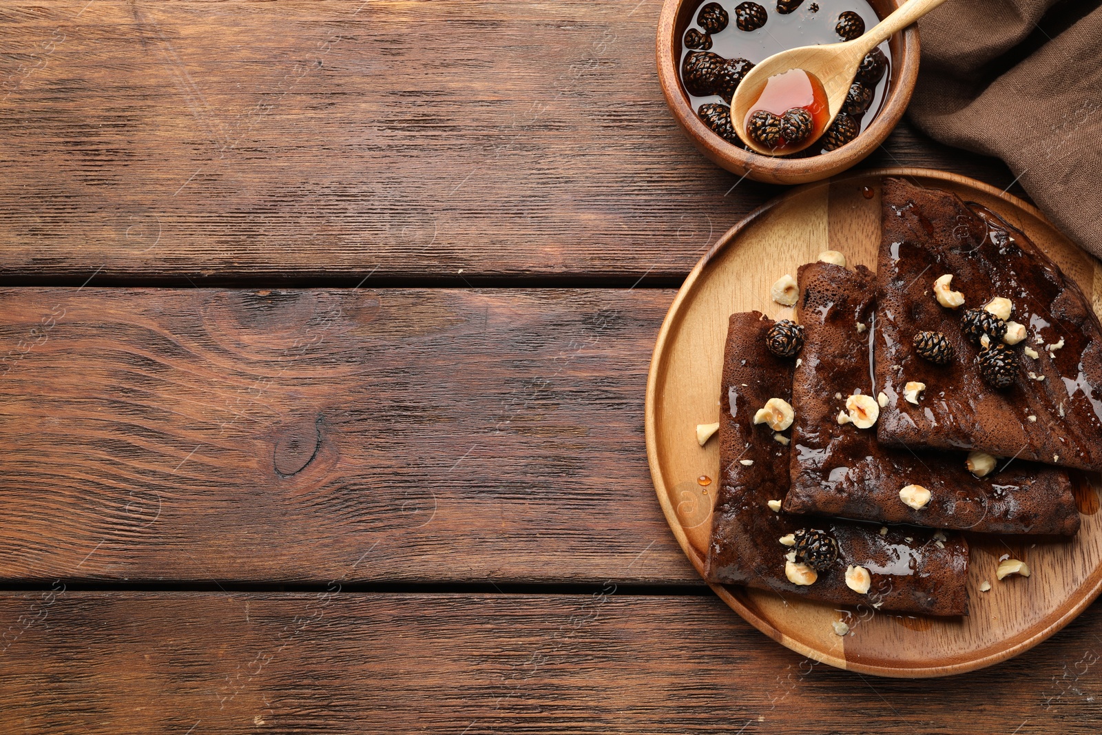 Photo of Delicious chocolate crepes with pine cone jam and nuts on wooden table, flat lay. Space for text