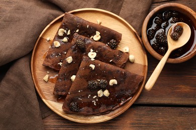 Photo of Delicious chocolate crepes with pine cone jam and nuts on wooden table, flat lay