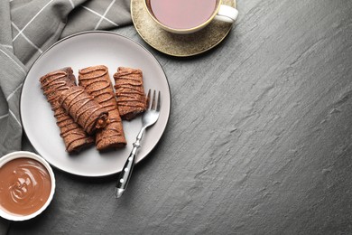 Photo of Delicious chocolate crepes with sweet paste, nuts and tea on black table, flat lay. Space for text